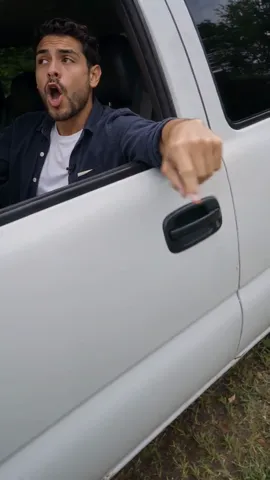 A bearded man at the wheel of a white pickup holding a white pen at his chest